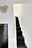 Gemauerter Treppenaufgang mit schwarz aufgemaltem Läuferband; Holztür mit marokkanischem Beschlag und gehämmerte Metallschalen an der Wand