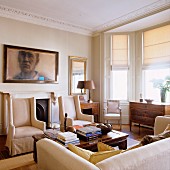 Living room with elegant, light colored armchairs in front of a wall with a portrait; decorative frieze on the ceiling and bay window