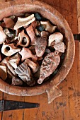 Small ceramic figurines in clay bowl on rustic wooden surface with metal fittings