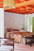 Ceiling structure painted orange above double bed with floral bed linen