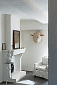 Armchair with loose cover in front of open fireplace and animal mask on wall in renovated, Mediterranean country house