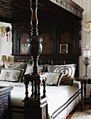 Stack of decorative pillows on a canopy bed with carved posts and colonial style, dark wood canopy