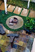 Gestalteter Garten mit Feuerstelle auf Kreisfläche und Kunstobjekte auf gefliestem Terrassenboden
