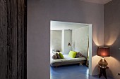 Blick durch Maueröffnung auf puristisches Schlafzimmer mit lindgrünen Kissen auf Doppelbett