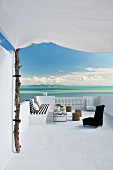 Afrikanische, niedrige Sessel und Sonnensegel an Baumstamm auf Terrasse mit traumhaftem Meerblick