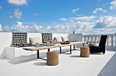 Schwarzweiss karierte Decken auf gemauerter Bank und rustikaler Holztisch mit Basthockern auf Terrasse am Meer