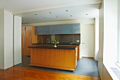 View of kitchen island with wooden fronts and fitted cupboards through floor-to-ceiling open doorway