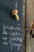Handwritten menu and fresh penny bun mushroom hanging against blackboard in kitchen