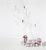 Zweig mit Weihnachtskugeln in einer Vase und in Zeitungspapier verpackte Geschenke