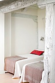 Elegante Einzelbetten in Nische eines rustikalen Schlafzimmers mit geweisselter Holzkonstruktion