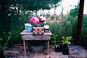 Old tins and summer bouquet in bucket on rustic wooden table in work space on terrace in cottage garden