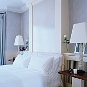 Doppelbett mit weisser Bettwäsche zwischen Nachttischen mit Tischleuchten und weißem Lampenschirm in traditionellem, elegantem Schlafzimmer