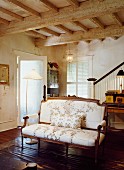 Antique couch with floral upholstery in interior with rustic, wood-beamed ceiling