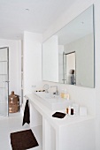 Minimalist white bathroom with large mirror above washstand and dark, contrasting towels