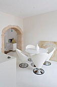 Dining area with designer shell chairs in white minimalist room with historical arched doorway