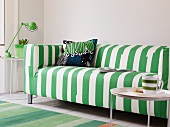 Side table with a cup in front of a modern green and white striped couch in front of a wall