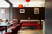 Interior of an Asian restaurant - assorted seating areas some with place settings in front of a dark wooden wall and red lanterns hanging from the ceiling