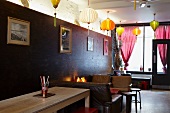 Innenraum eines asiatischen Restaurants - verschiedenfarbige Lampions an Decke und Sitzplätze vor dunkler Holzwand