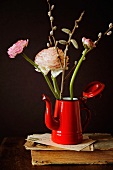 Ranunculus and pussy willow in red coffee pot on old book