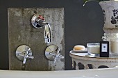 Designer, wall-mounted tap fittings on concrete panel and toiletries on vintage table