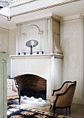 Antique-style upholstered armchairs in front of open fireplace in elegant interior