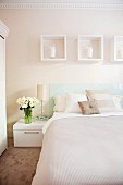 Double bed with bedspread and scatter cushions in pastel, natural shades below white decorative picture frames on wall in delicate cream
