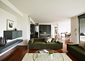 Runder Couchtisch auf flokatiartigem Teppich und grüne Couchgarnitur in Loungeecke mit zwischen Wand eingespanntem Regalboden in offenem Wohnraum