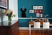 Desk and two chairs against blue wall; bouquet on traditional chest of drawers in foreground
