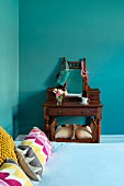 Bed with colourful scatter cushions and antique dressing table and stool in turquoise bedroom