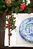 Place setting with blue and white crockery on pulled thread work place mat and small posy with pinecone and red berries as festive table decoration