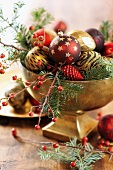 Christmas baubles on fir branches and sprigs of berries in gilt bowl