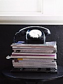 Retro telephone on stack of magazines against black-painted wall
