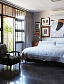 Double bed with white, lace bedspread below collection of modern artworks on wall in traditional setting