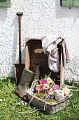 Rustikales Stillleben vor einer Hauswand mit Rosenbouquet und Schnurknäuel in Weidenkorb