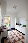 Moderne, weiße Einbauküche mit ausgefallenem Fliesenmosaik und breiter Glastür in den Garten