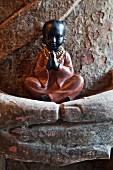Small figurine of praying boy held in folded hands of larger statue