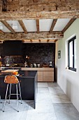 Modern designer kitchen with bar stools at breakfast bar below renovated wood-beamed ceiling in converted stable