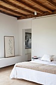 Doppelbett mit einfachem Holzhocker als Nachttisch und Aktzeichnung neben türlosem Durchgang zum angrenzenden Raum