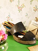 Old ladies shoe used as a pencil holder on a green surface in front of floral wallpaper