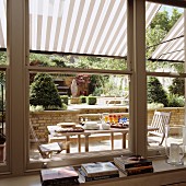 View through sash windows onto terrace with set table below striped awning