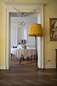View into a dining room with a round table, in the foreground an old floor lamp with a fabric shade