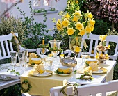 Gelbe Tischdekoration mit fächerförmig gefalteten Servietten, Narzissenstrauss und Weidenkränzchen
