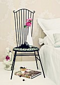 Pink roses of variety ' Yves Piaget' on figurine of woman & in vase on romantic metal chair next to bed
