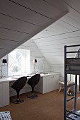 Desk and black, designer swivel chairs below window in attic room