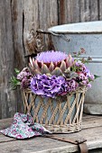 Arrangement of artichoke flower, hydrangeas and flowering marjoram in wicker basket