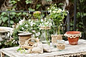 Hand-sewn hessian sachets and glass vessels with knitted covers on rustic garden table