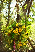 Wreath of summer flowers, mainly yellow, against blurred tapestry of trees