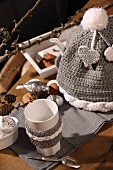 Beaker with knitted trim next to hand-crocheted tea cosy and Christmas decorations on table