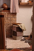 Laundry basket with knitted patchwork cover on bathroom mat and terracotta tiled floor in Mediterranean ambiance