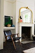 Vintage leather armchair next to open fireplace with gilt-framed mirror